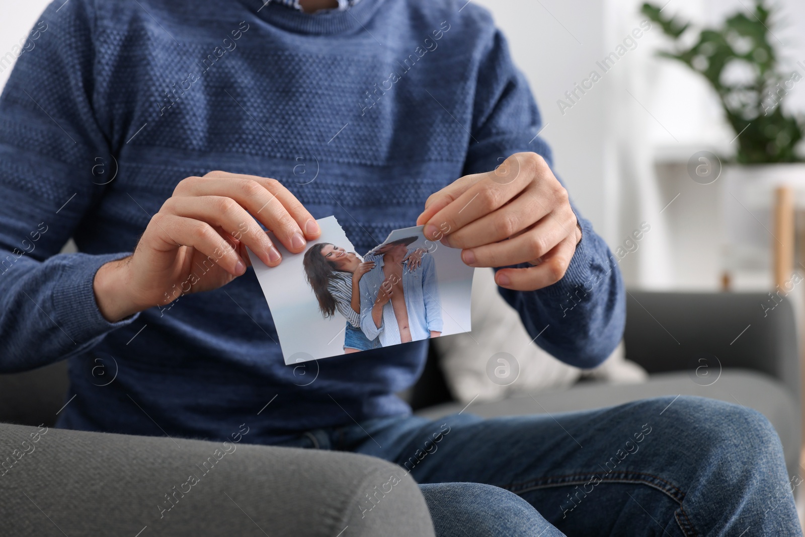 Photo of Man ripping photo on sofa indoors, closeup. Divorce concept