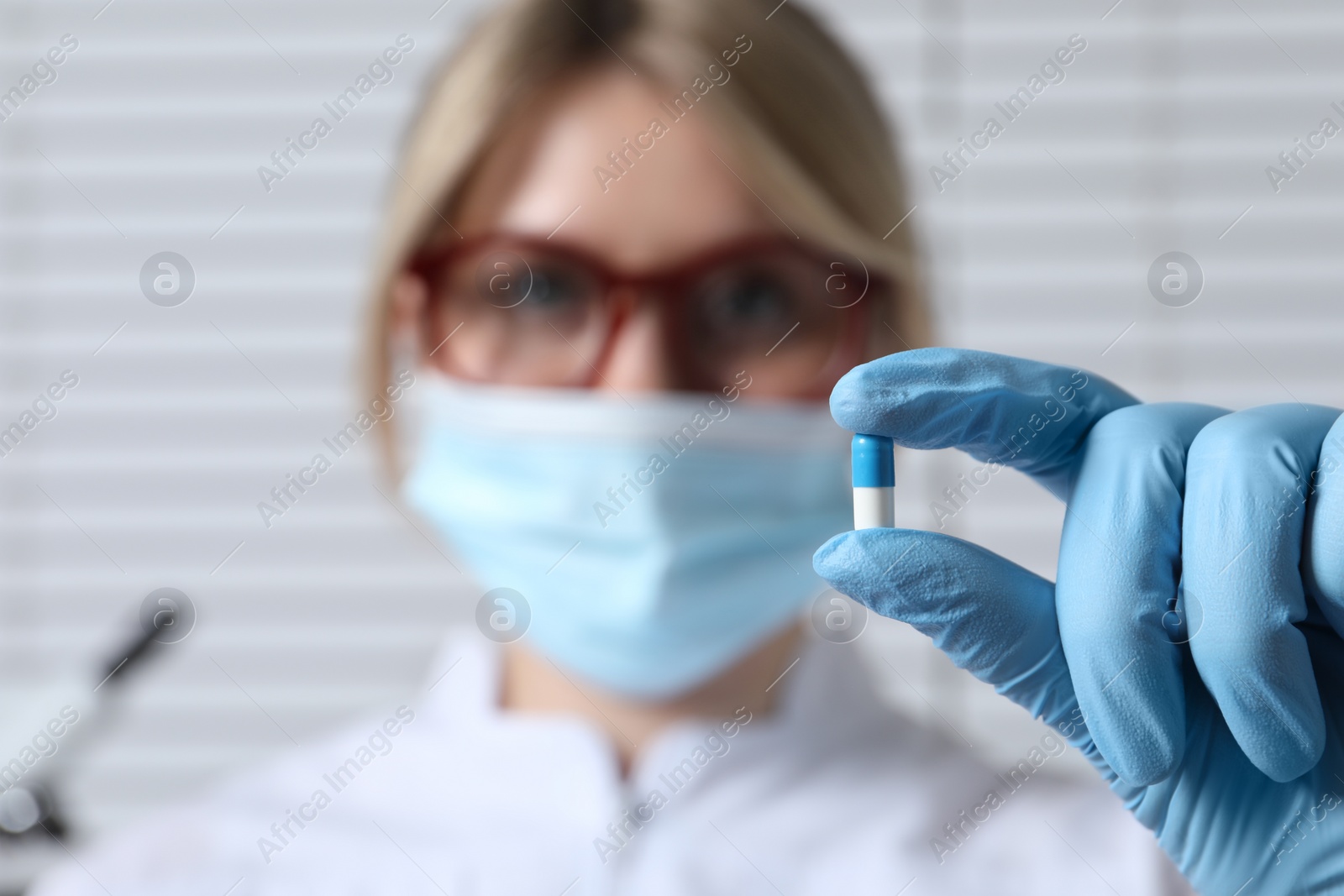 Photo of Doctor holding pill on light background, selective focus. Space for text