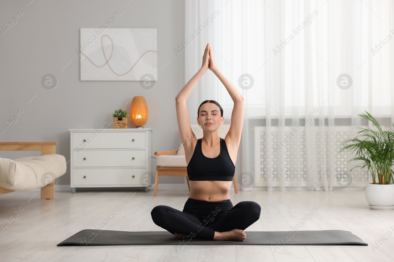 Photo of Beautiful young woman practicing Padmasana on yoga mat at home. Lotus pose