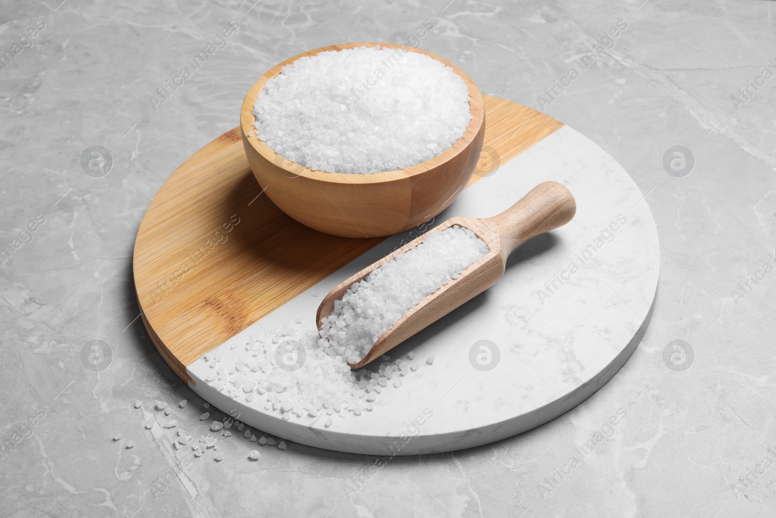 Photo of Wooden bowl and scoop with natural sea salt on light grey table