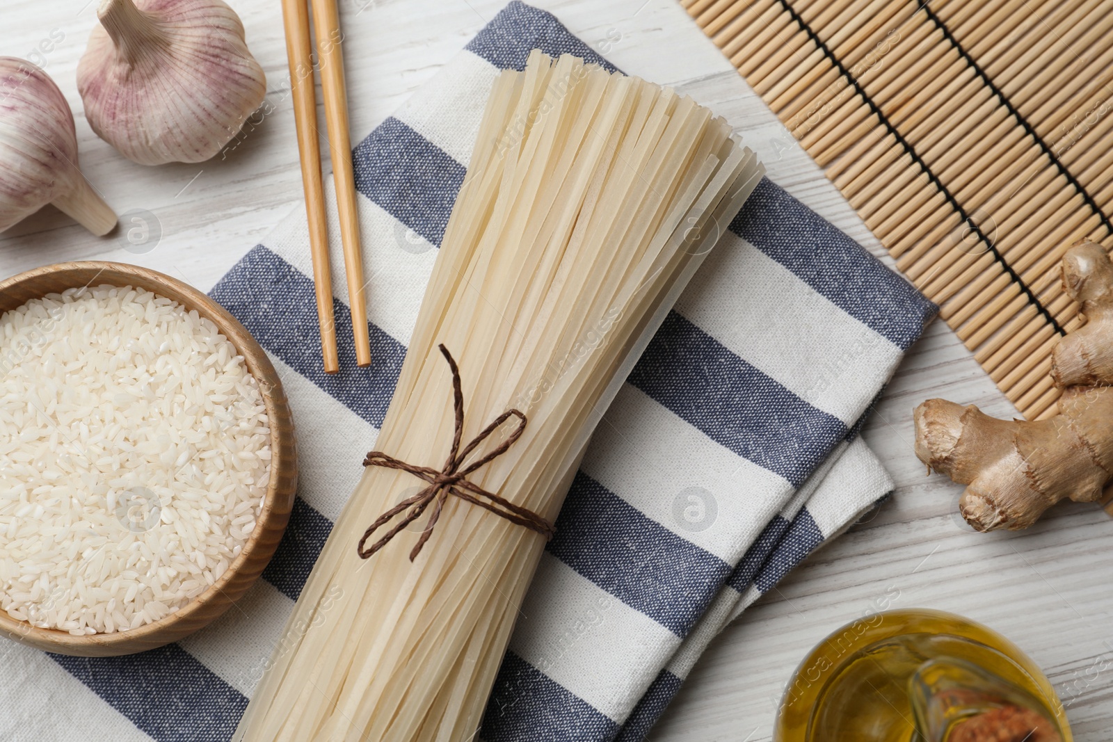 Photo of Bowl with dried rice noodles and ingredients on white wooden table, flat lay