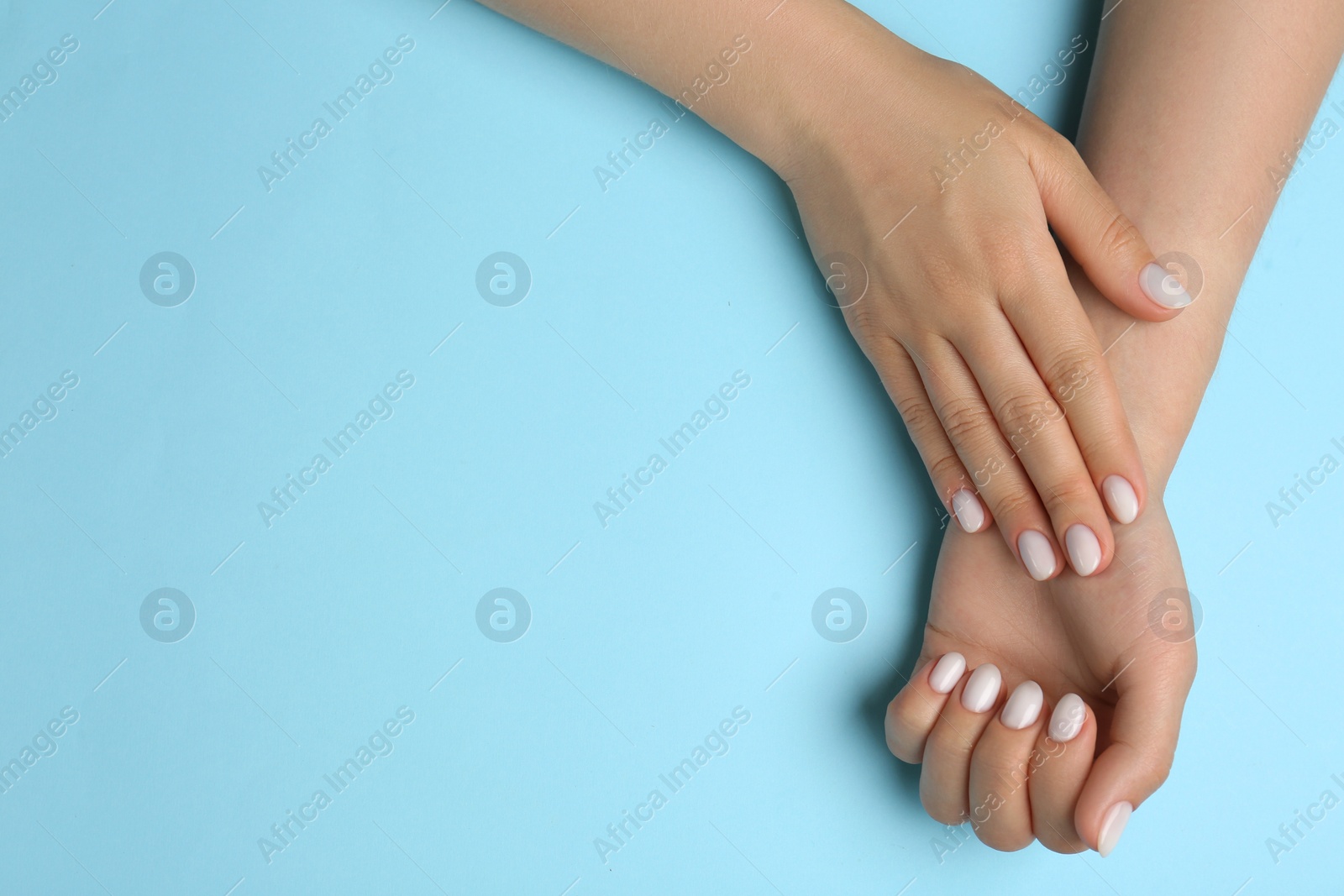 Photo of Woman showing her manicured hands with white nail polish on light blue background, top view. Space for text