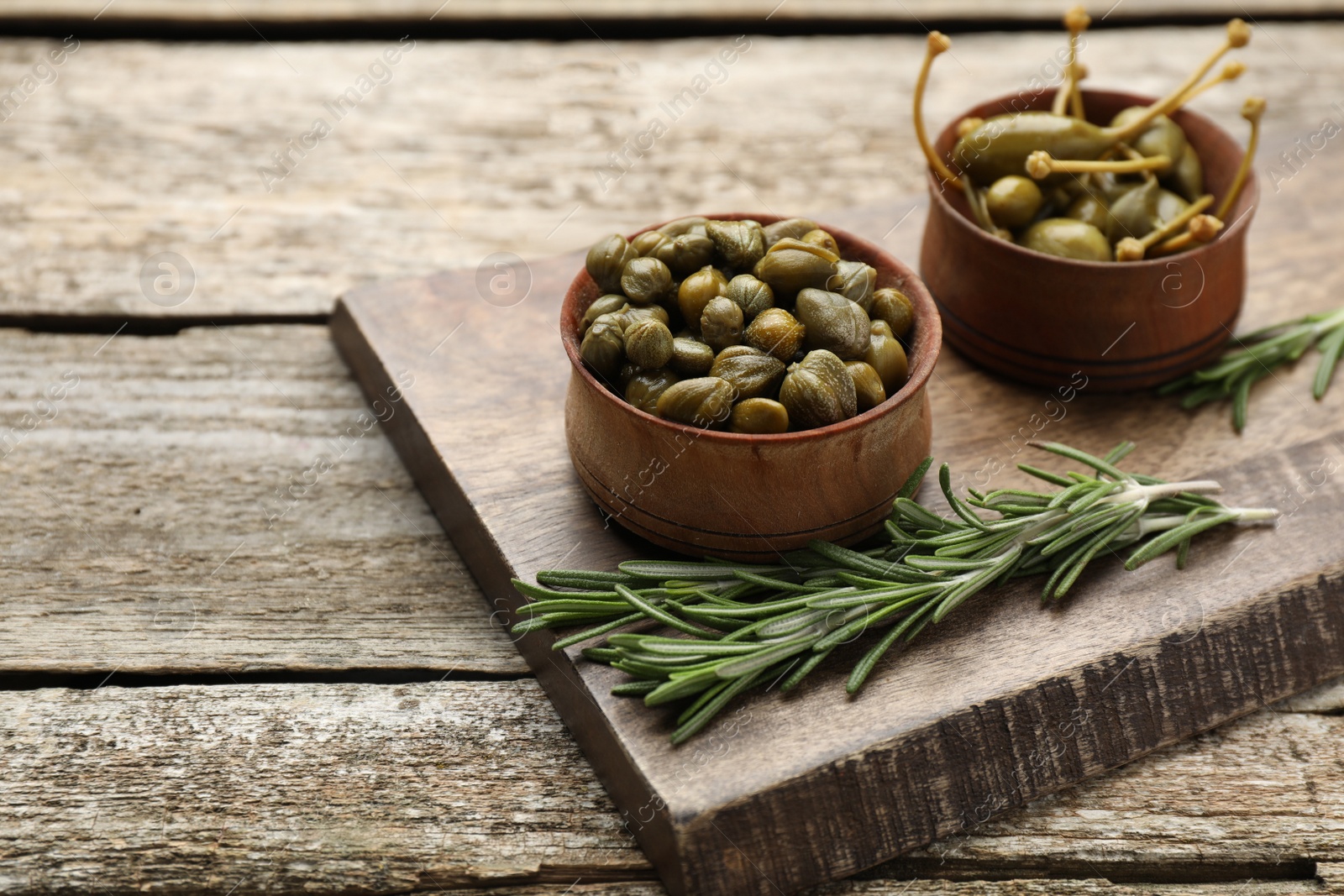 Photo of Delicious pickled capers and rosemary twigs on wooden table, space for text