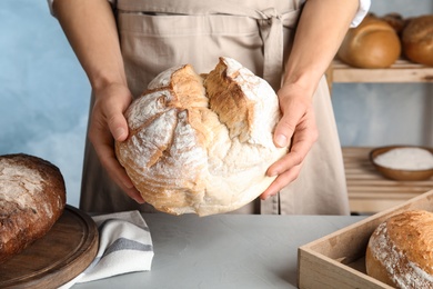 Baker holding loaf of bread over table indoors, closeup