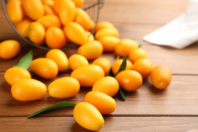 Photo of Fresh ripe kumquats with green leaves on wooden table