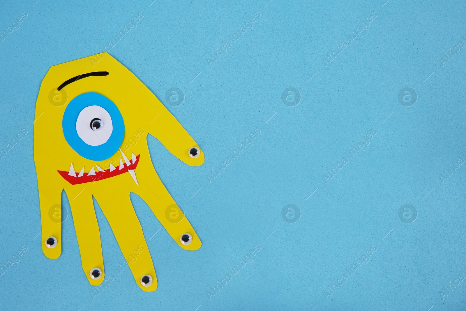 Photo of Funny yellow hand shaped monster on light blue background, top view with space for text. Halloween decoration
