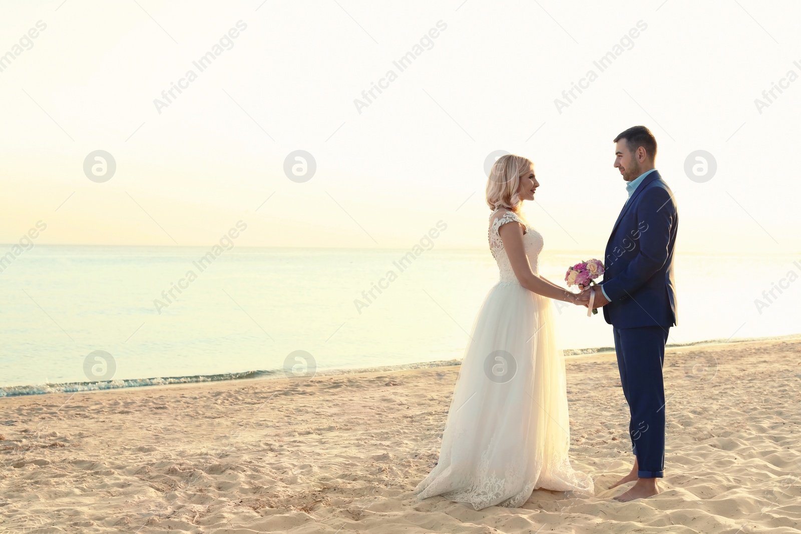 Photo of Wedding couple holding hands together on beach. Space for text