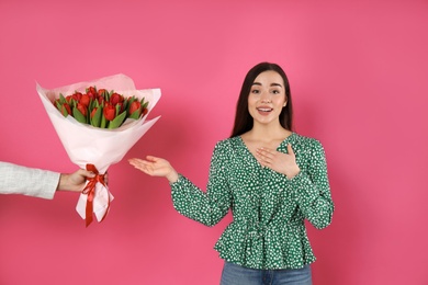 Photo of Happy woman receiving red tulip bouquet from man on pink background. 8th of March celebration