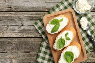 Photo of Delicious sandwiches with cream cheese and basil leaves on wooden table, top view. Space for text