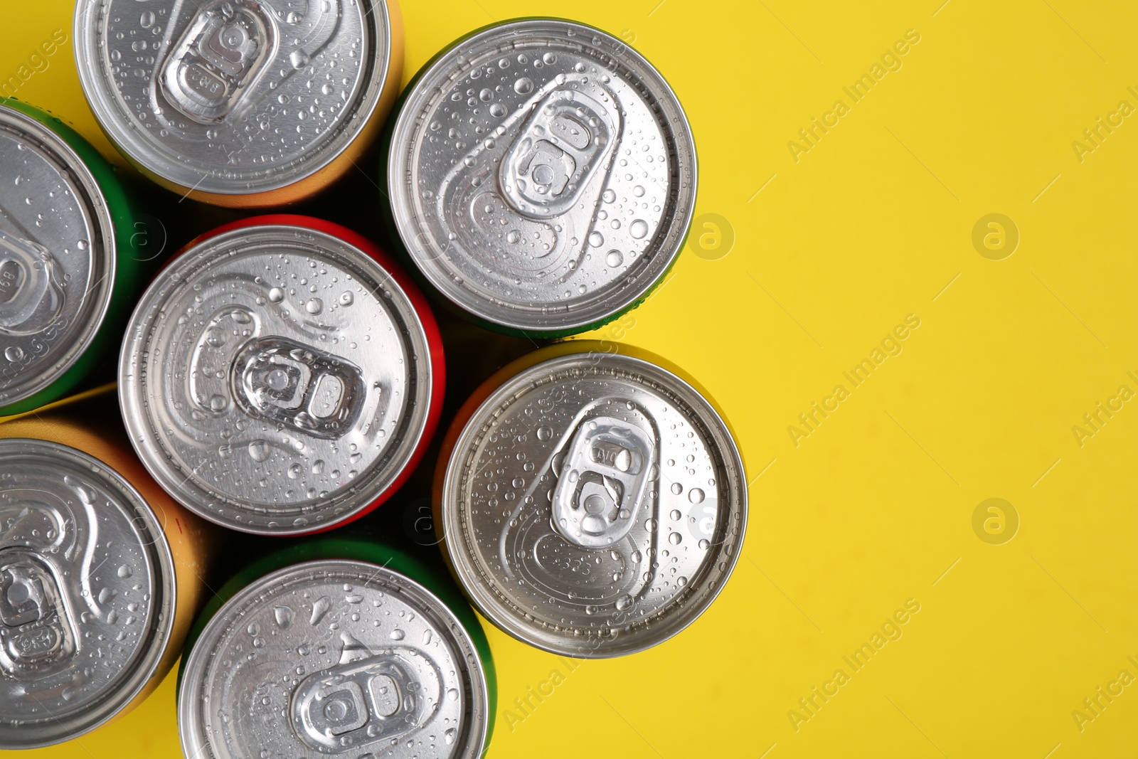 Photo of Energy drinks in wet cans on yellow background, top view. Space for text