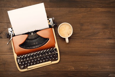 Vintage typewriter and cup of coffee on wooden table, flat lay. Space for text