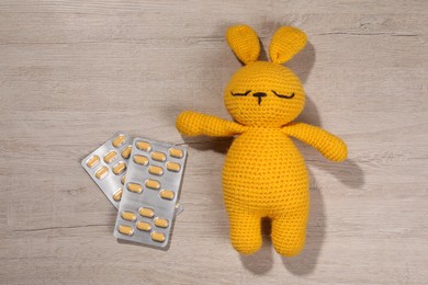 Photo of Toy bunny and pills on wooden background, flat lay