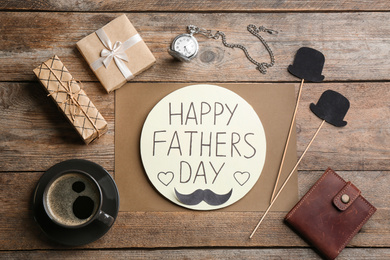 Greeting card with phrase HAPPY FATHER'S DAY, coffee and wallet on wooden table, flat lay