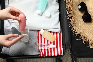 Photo of Woman putting small bottle with personal care product into plastic bag, closeup. Cosmetic travel kit