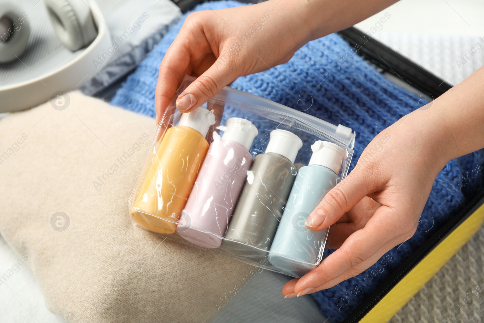 Photo of Woman with plastic bag of cosmetic travel kit packing suitcase, closeup