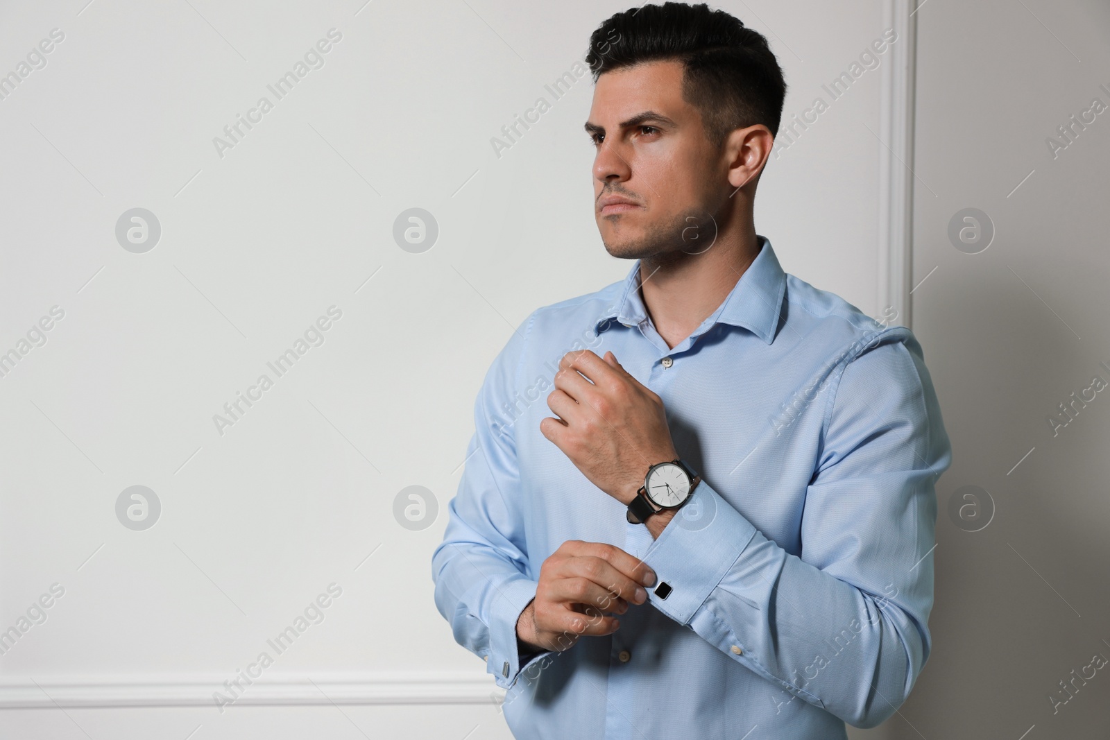 Photo of Handsome stylish man putting on cufflink against grey wall. Space for text