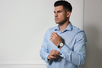 Photo of Handsome stylish man putting on cufflink against grey wall. Space for text