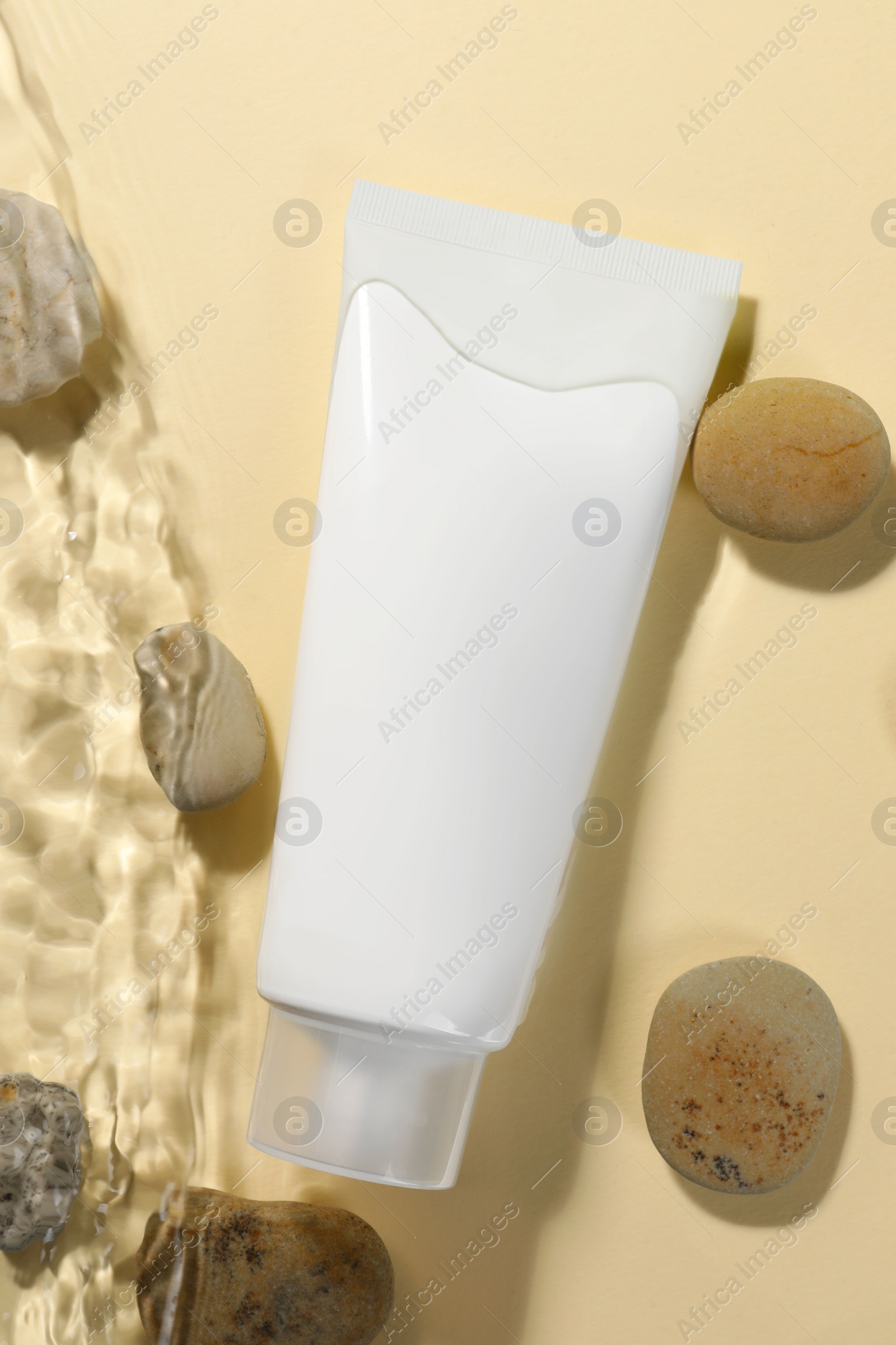 Photo of Tube of face cleansing product and stones in water against beige background, flat lay