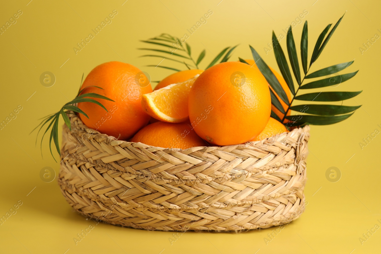 Photo of Fresh oranges in wicker basket on yellow background, closeup