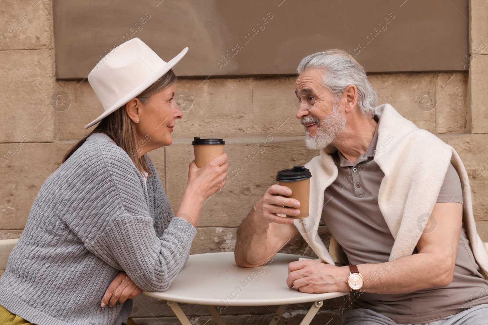 Photo of Affectionate senior couple sitting in outdoor cafe and drinking coffee