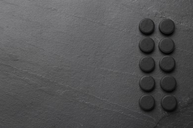 Photo of Activated charcoal pills and space for text on black table, flat lay. Potent sorbent