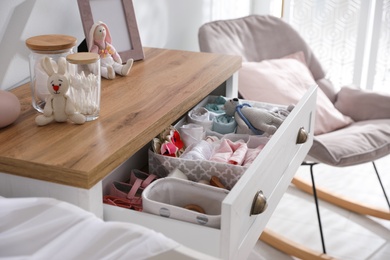 Photo of Modern open chest of drawers with baby clothes and accessories in room, closeup