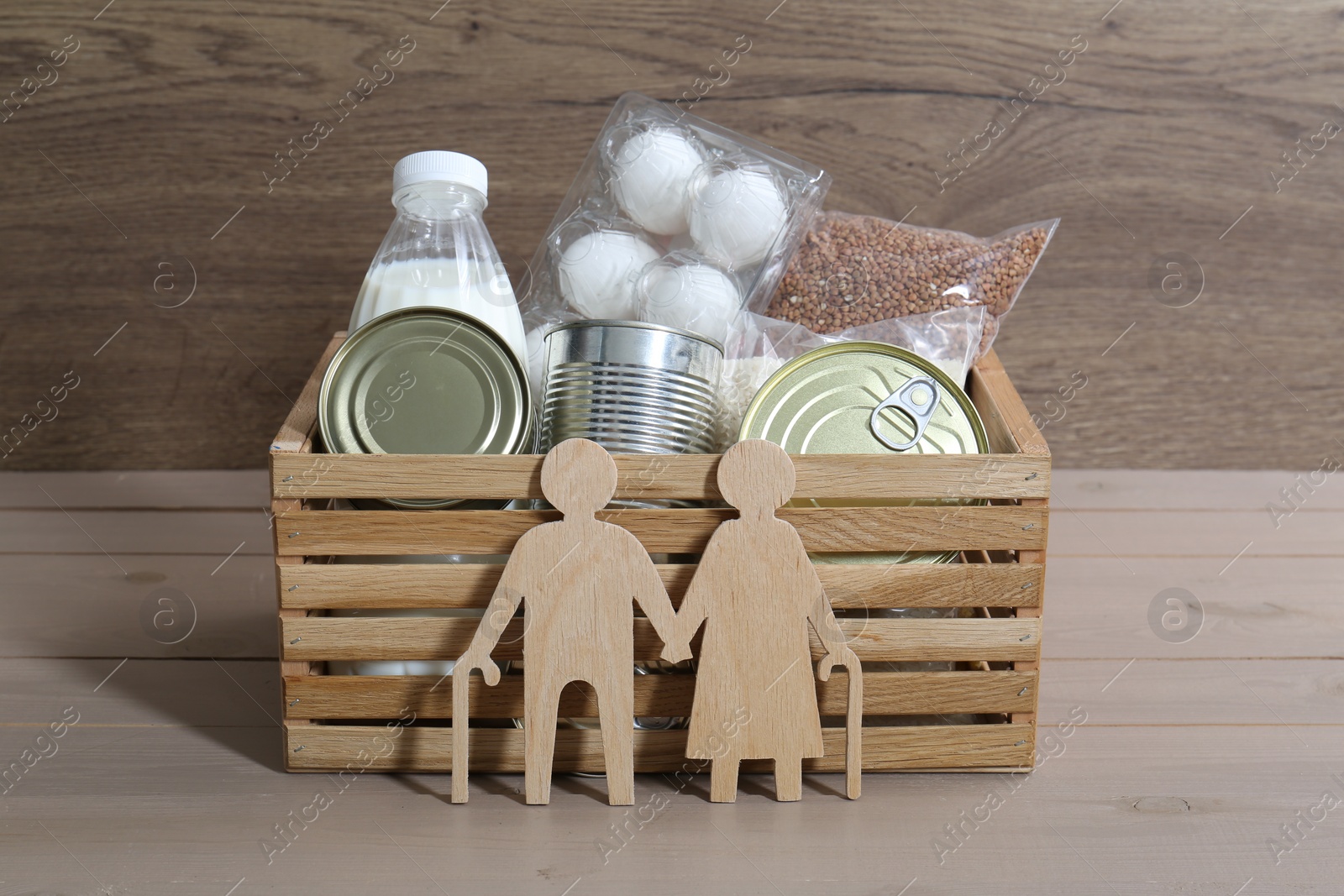 Photo of Humanitarian aid for elderly people. Donation box with food products and figure of senior couple isolated on wooden table
