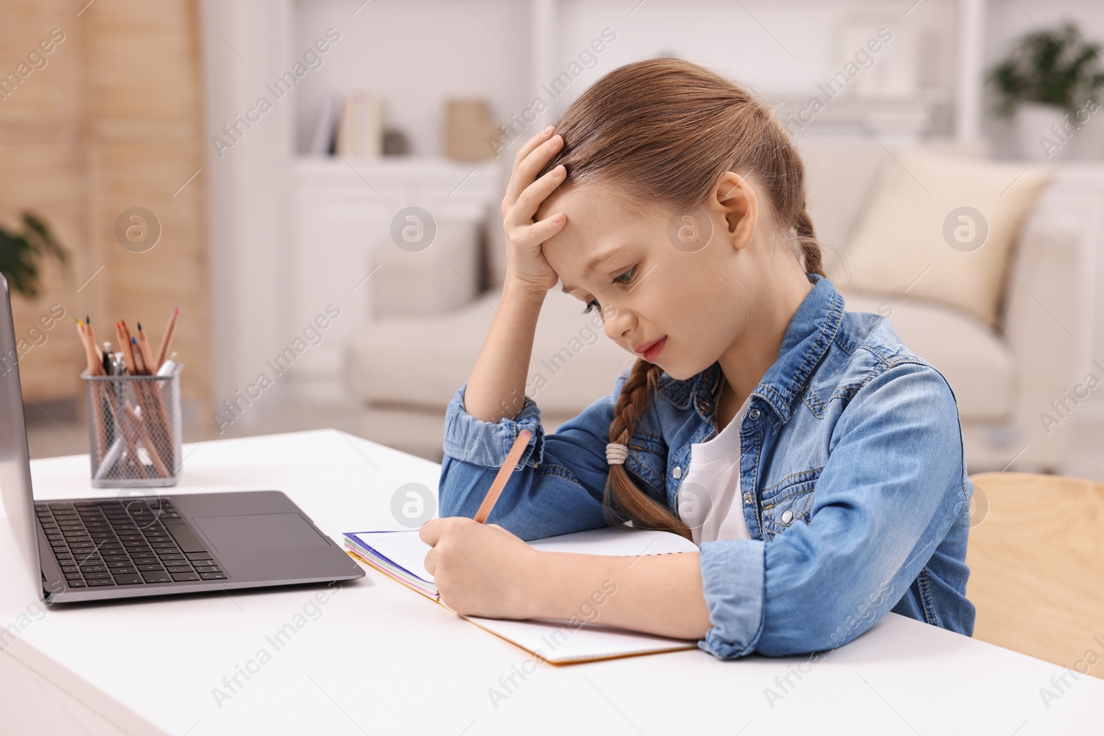 Photo of Little girl suffering from headache while doing homework at home