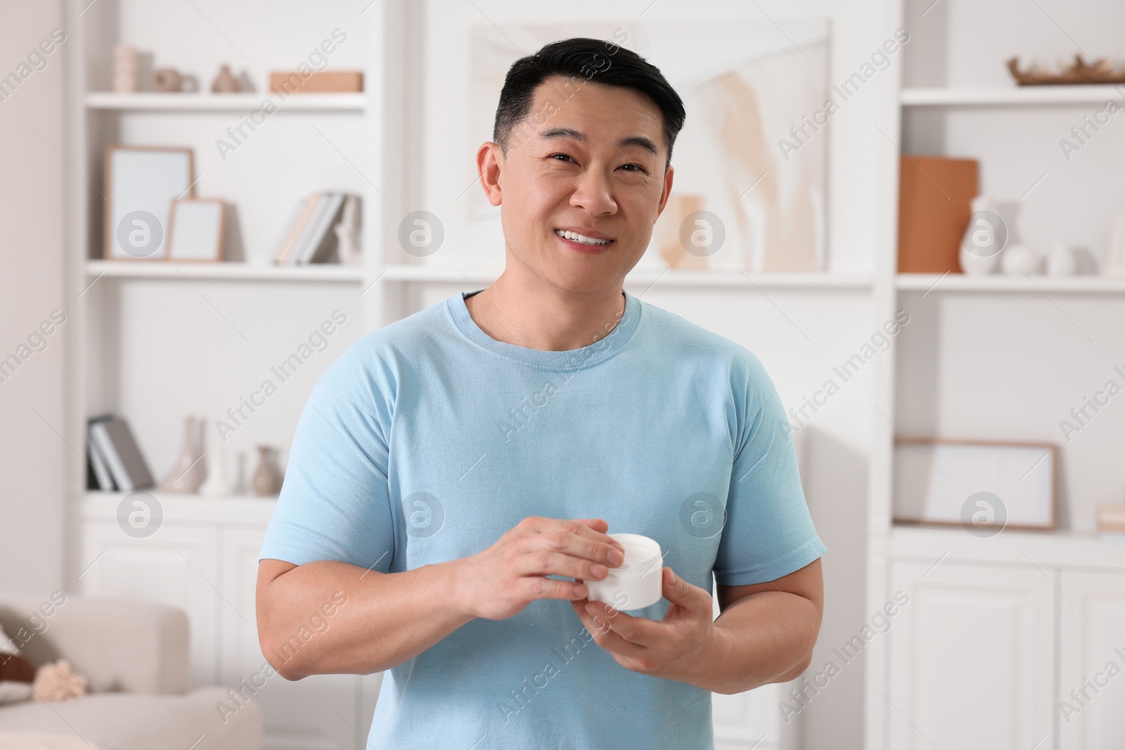 Photo of Handsome man with jar of body cream at home