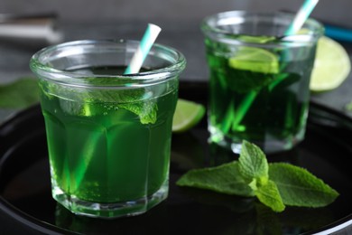 Photo of Delicious mint liqueur with green leaves and lime on black tray, closeup