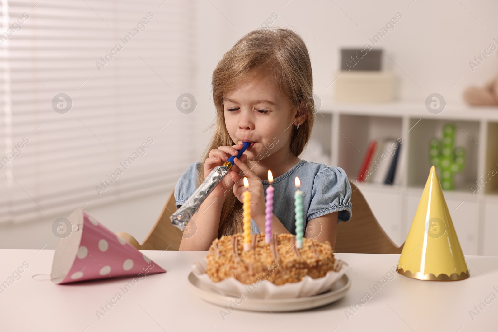 Photo of Birthday celebration. Cute girl holding blower at table with tasty cake indoors