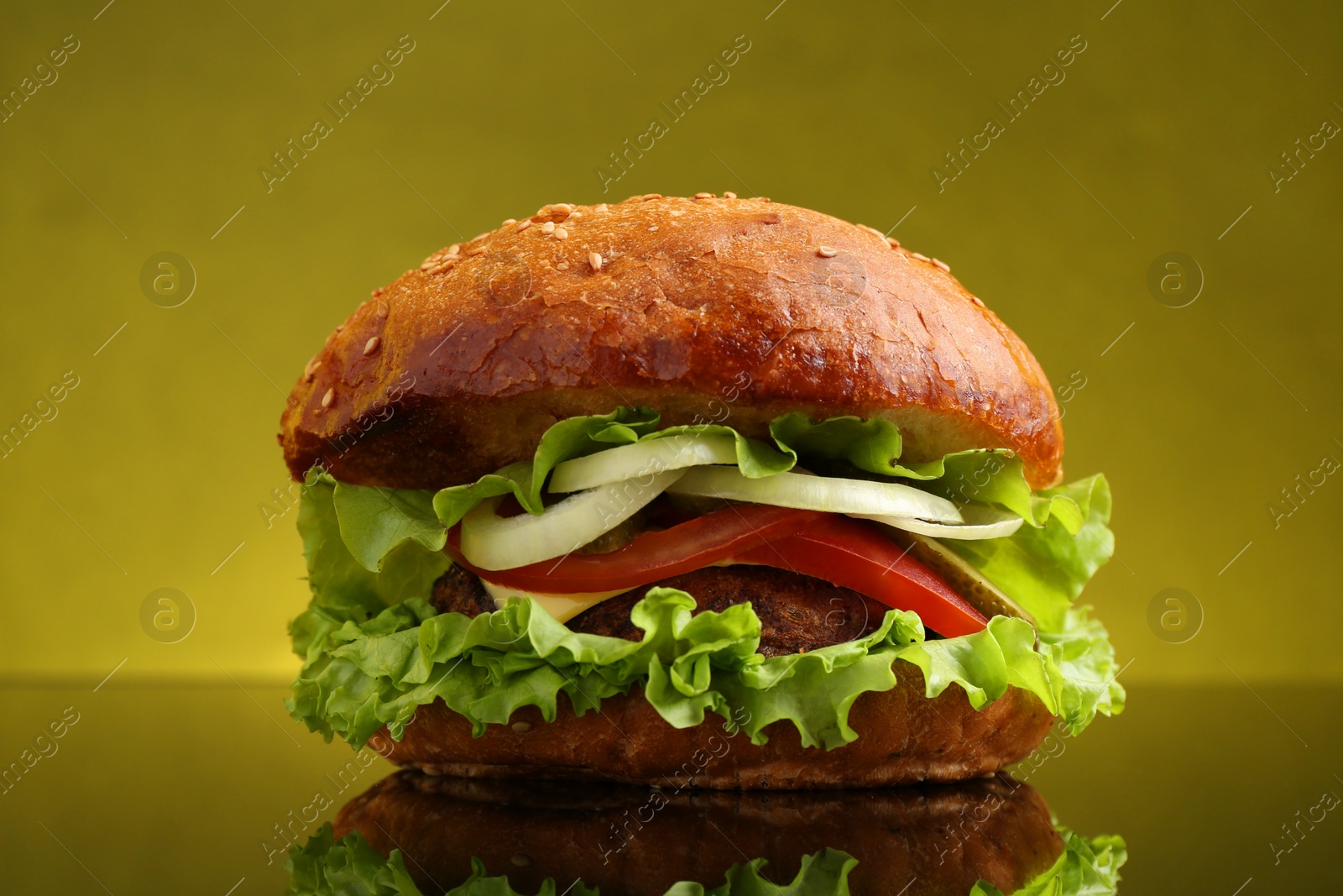 Photo of Delicious vegetarian burger on mirror surface against olive background