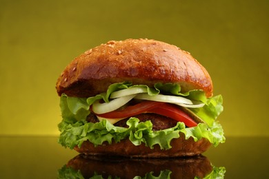 Photo of Delicious vegetarian burger on mirror surface against olive background