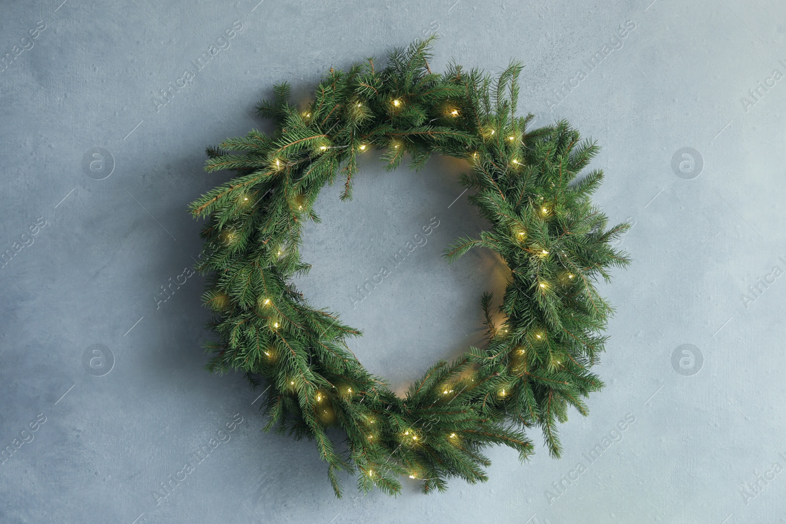 Photo of Beautiful Christmas wreath with festive lights on light blue wall