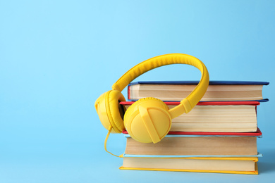 Photo of Books and modern headphones on light blue background. Space for text