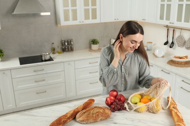 Photo of Woman with string bag of fresh fruits, baguettes and bread on light marble table, above view