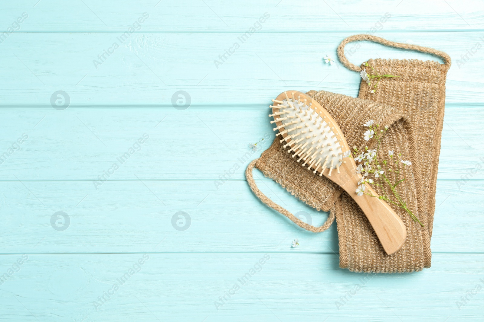 Photo of Hair brush, bast wisp and small white flowers on light blue wooden background, flat lay. Space for text