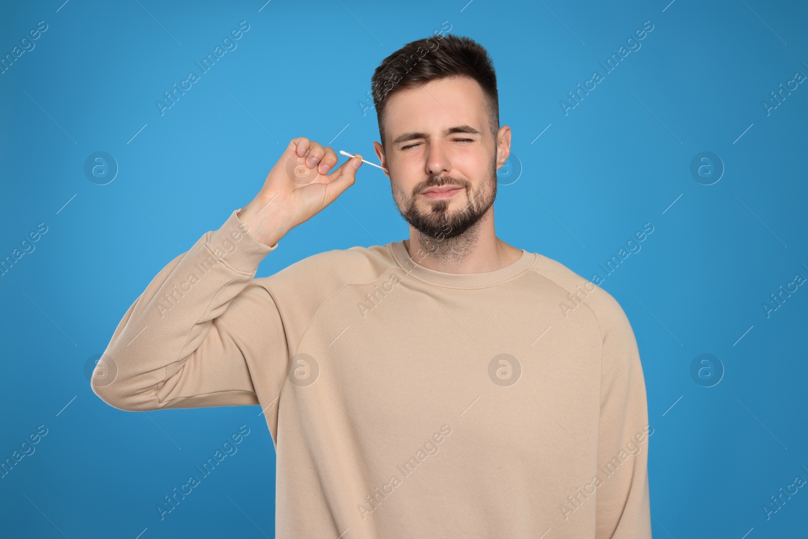 Photo of Young man cleaning ear with cotton swab on light blue background