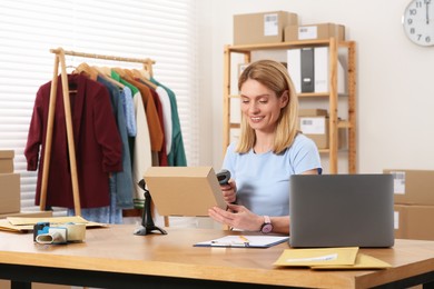 Photo of Seller with scanner reading parcel barcode at table in office. Online store