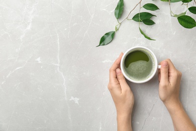 Woman with cup of matcha tea and leaves at table, top view