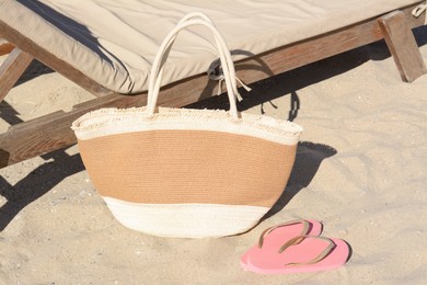 Photo of Straw bag and flip flops near wooden sunbed on sandy beach. Summer accessories