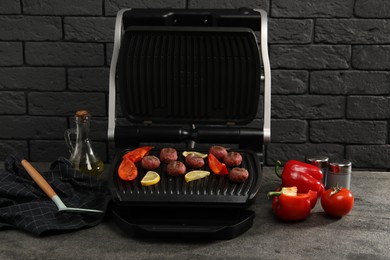 Photo of Electric grill with meat balls, bell peppers and lemon on grey textured table