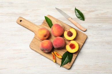 Photo of Fresh ripe peaches with green leaves and knife on light wooden table, above view