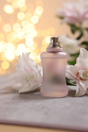 Photo of Bottle of perfume and beautiful lily flowers on table against beige background with blurred lights, closeup