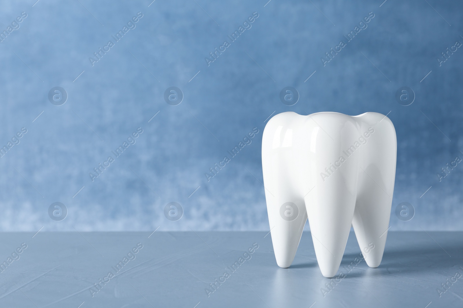 Photo of Ceramic model of tooth on table against color background. Space for text