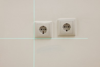 Photo of Using cross line laser level for accurate installation of outlet in white wall