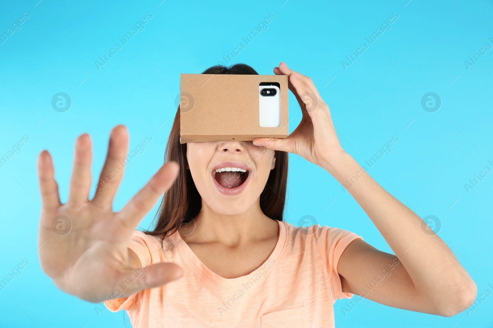 Photo of Young woman using cardboard virtual reality headset on color background