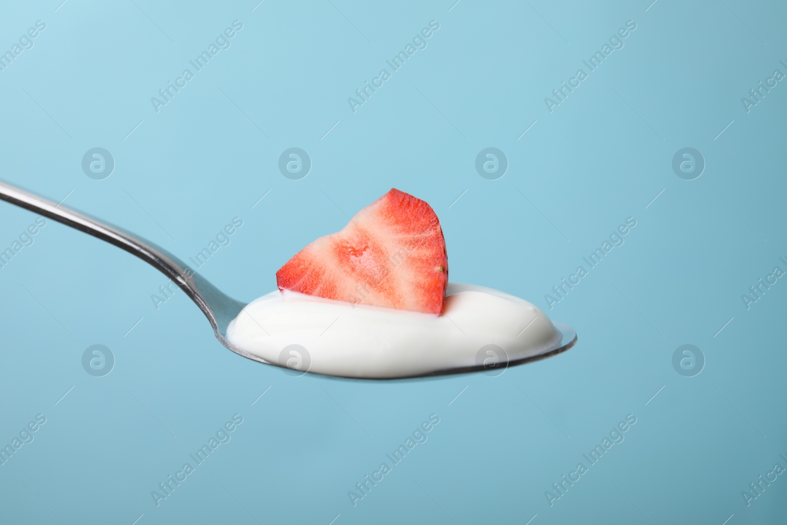 Photo of Delicious natural yogurt with fresh strawberry in spoon on light blue background