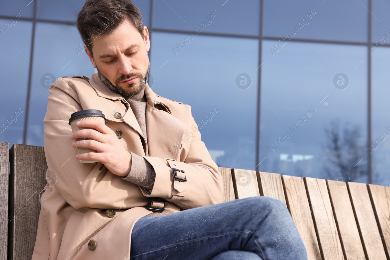 Photo of Tired man with cup of coffee sleeping while sitting on bench outdoors. Space for text