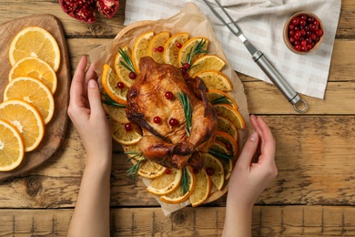 Photo of Woman holding baked chicken with orange slices at wooden table, closeup